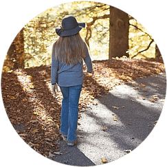 A woman with a hat taking a walk on a path with fallen leaves and trees