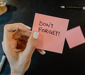 A feminine hand holding a pink sticky note that says don't forget